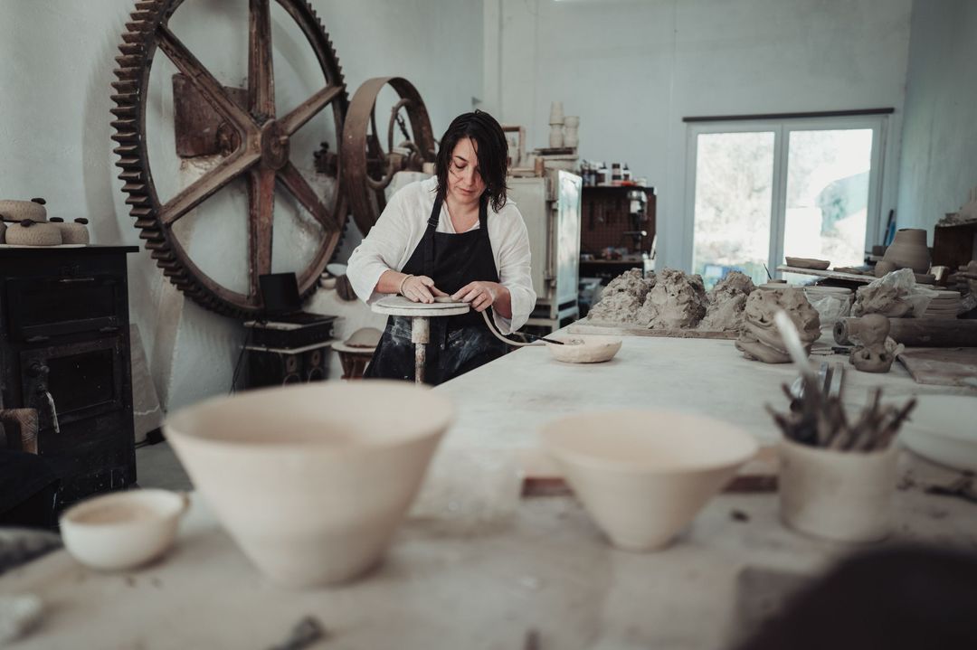 The studio with a large old iron gear wheel on the wall; Diana works at the back, unfired bowls stand in front
