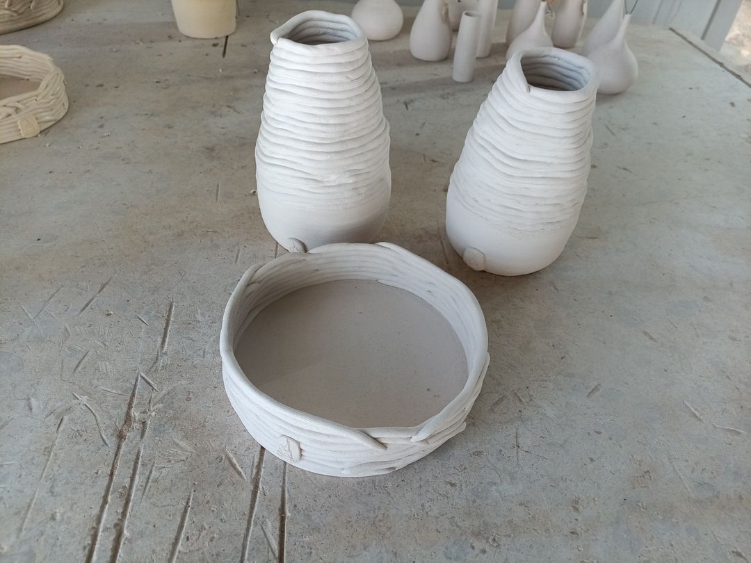 Two tall white vessels and a low round dish with visible coils of clay, on a work table, not yet fired