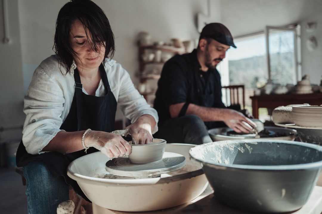 Diana and José throwing bowls at two potter's wheels side by side