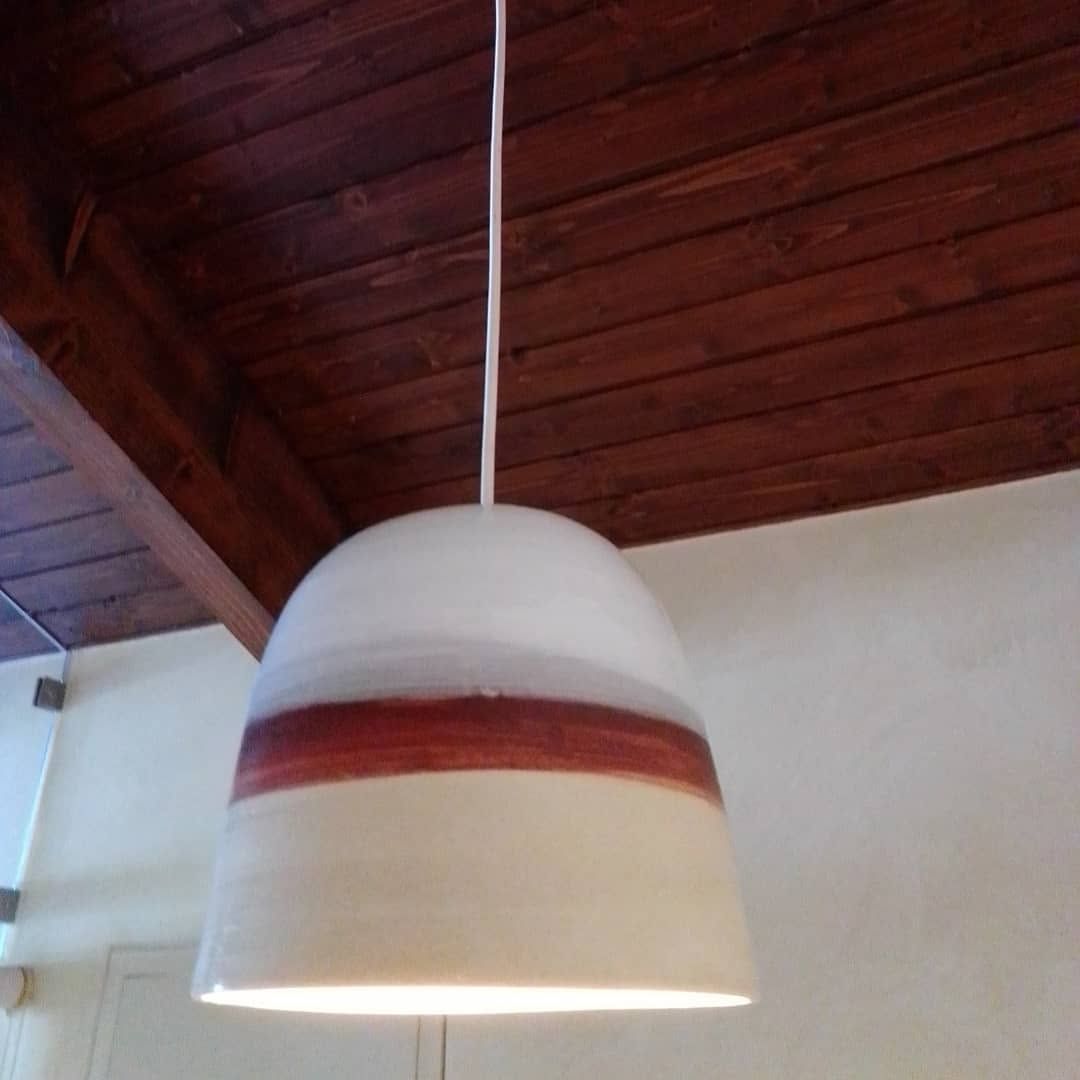 White ceramic pendant lamp with a red band, hanging from a wooden ceiling