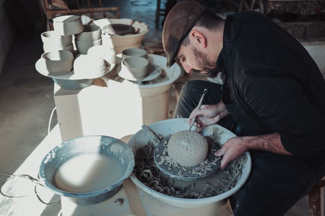 José carving a pattern into a round piece on the wheel, stacks of bowls behind him