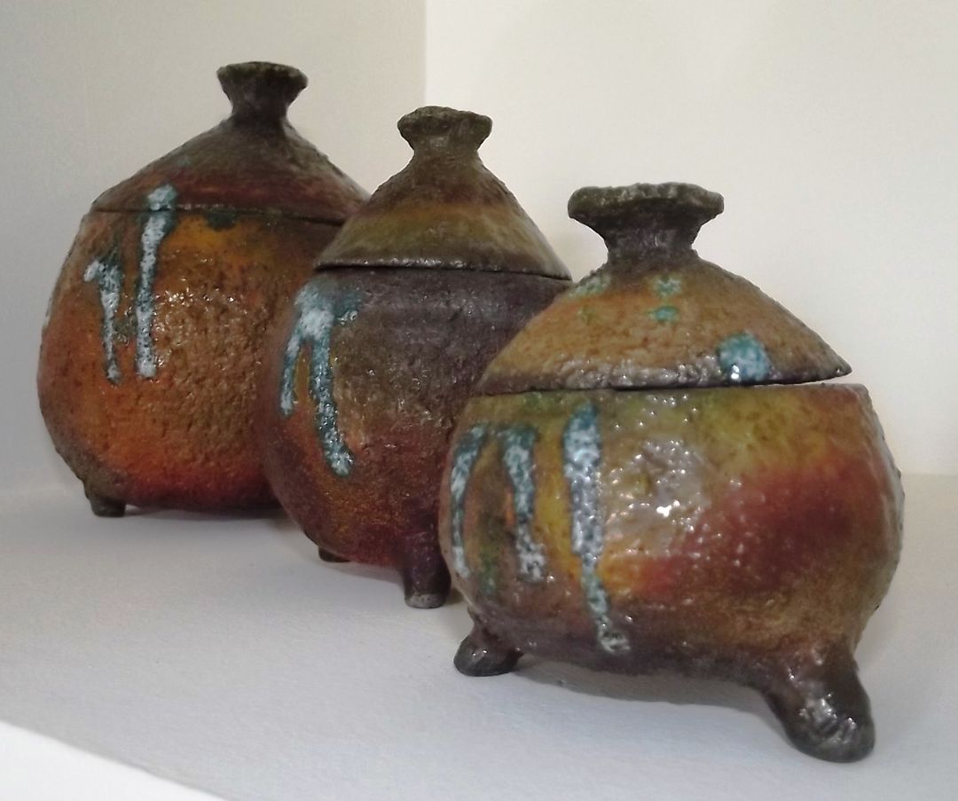 Three round raku jars on small feet, with lids and a shimmering copper and blue glaze