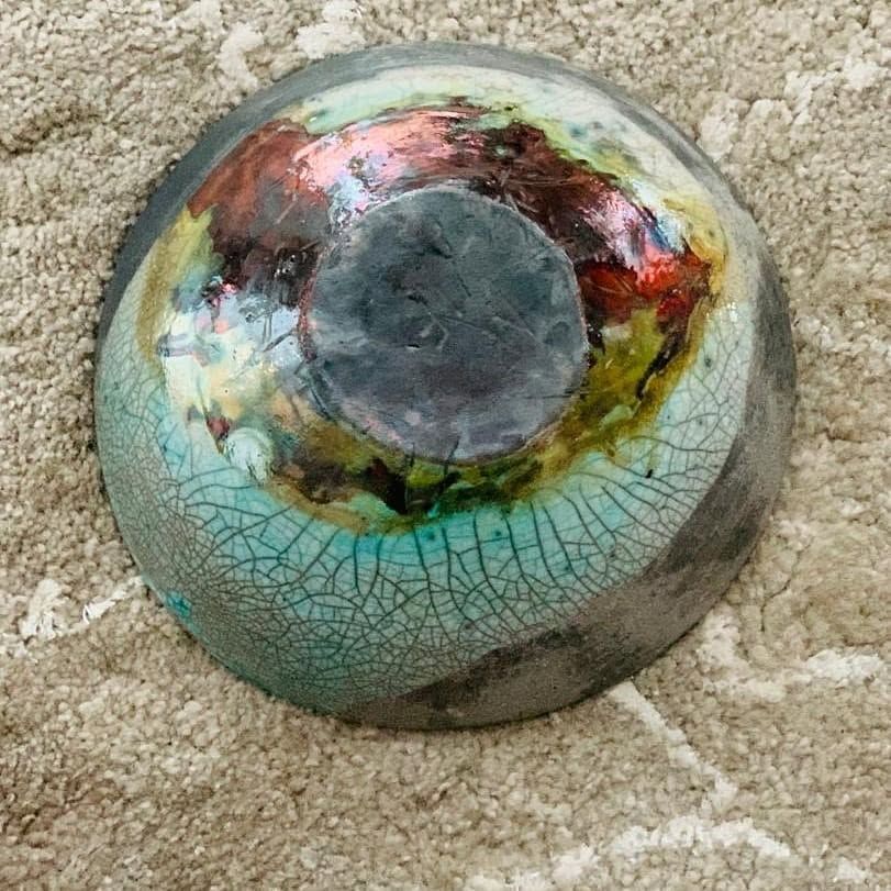 Round raku bowl seen from above, turquoise crackle glaze with red and gold patches and a dark smoked base