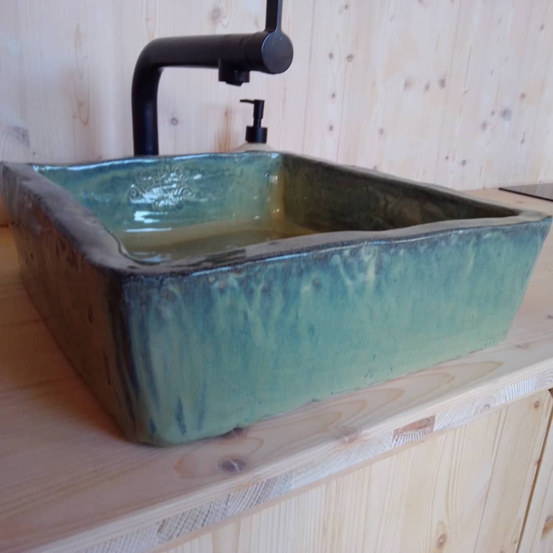 Square handmade washbasin with a deep turquoise glaze and a black tap, on a wooden counter